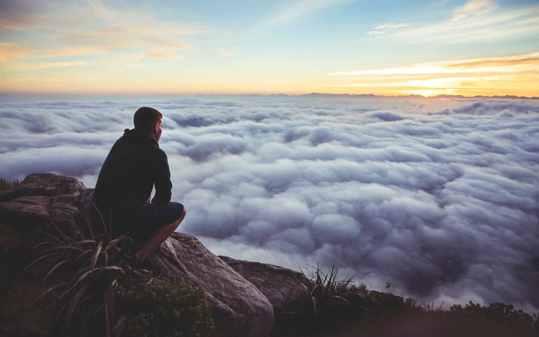 hombre sentado en montaña observando un mar de nubes